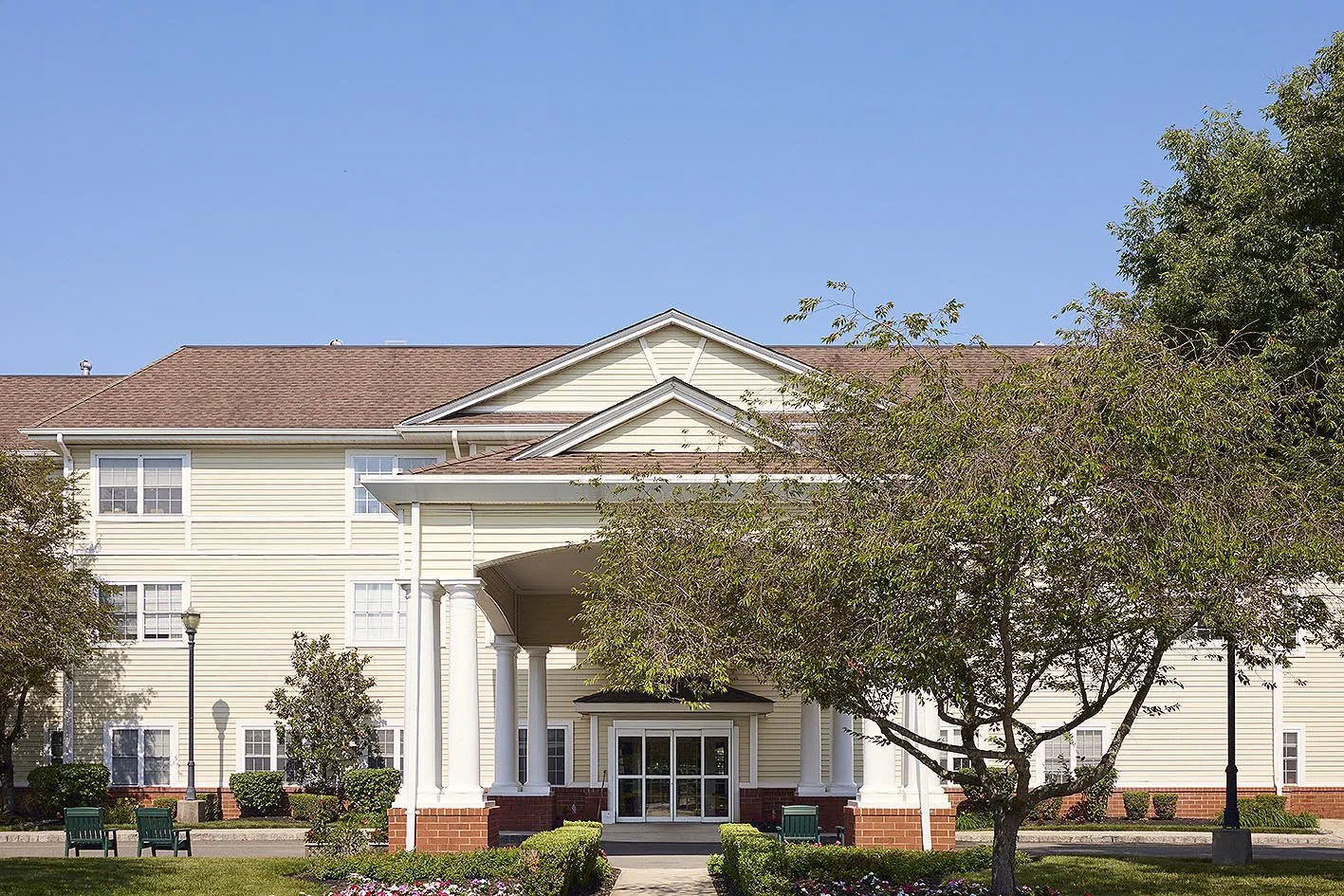 Front entrance of Brandywine Living at Pennington, a three-story building with a white-columned portico, under a blue sky.