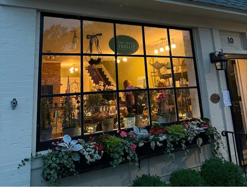 The Green Trellis storefront at dusk, with a lit shop window full of plants and gifts above an overflowing flower box.